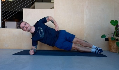 Man On Yoga Mat Showing Someone How To Do The Side Plank Exercise